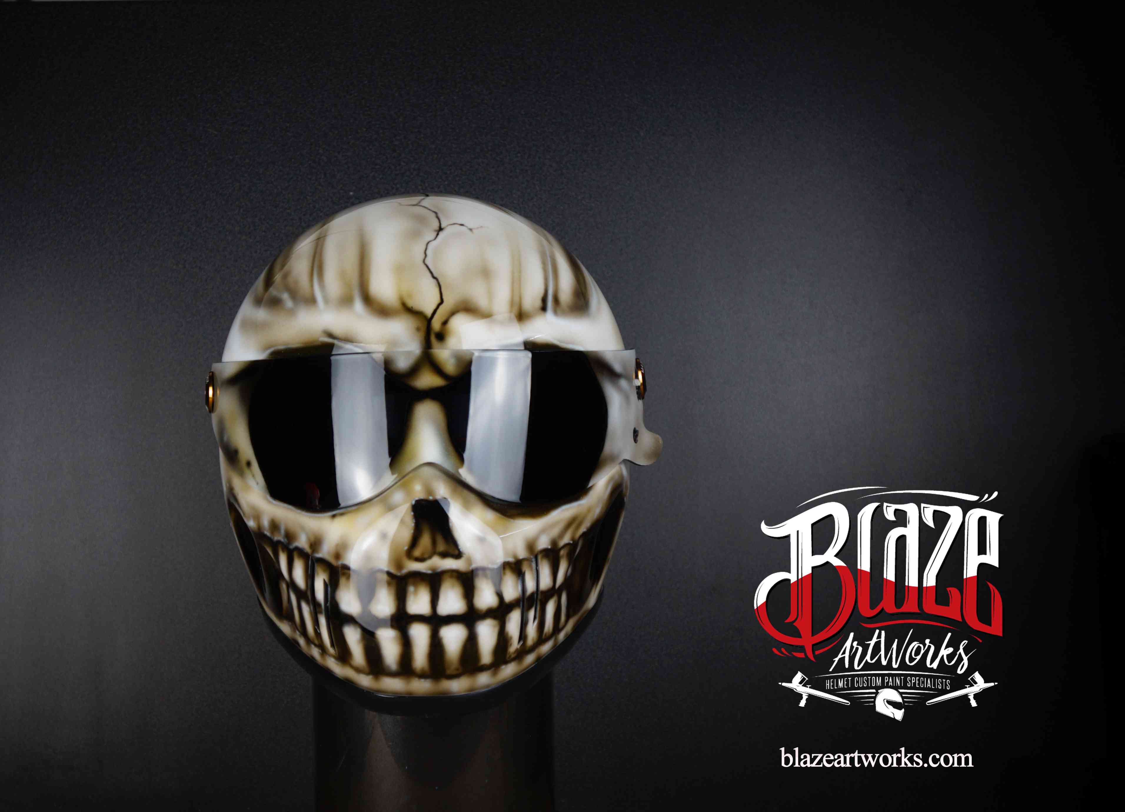 Cracked skull motorcycle helmet design with grinning teeth, bone-colored airbrush art on dark background with reflective visor